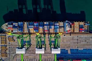 Post Image: Aerial view of a container ship anchored at a cargo port.