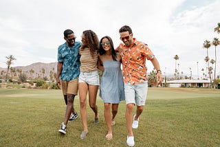 Four young men and women laughing and walking on grass in Palm Springs, California.