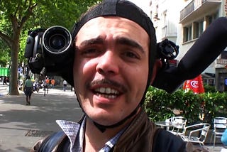 A mustache wearing man with a weird contraption around his head is seen smiling at the camera.