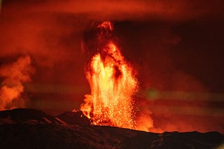 A fountain of orange-red lava shooting into the air during the nighttime.