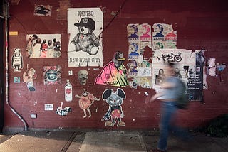 Photo showing a person walking in a motion blur past a wall with art posters.