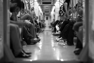 Black and white photo looking down the middle of a subway car with people’s legs on either side.