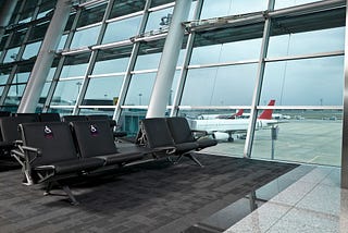 An airport gate waiting area with chairs and a large window with planes outside. Two chairs have a wheelchair icon.