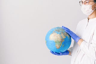 Person wearing a medical face mask and gloves holding a globe