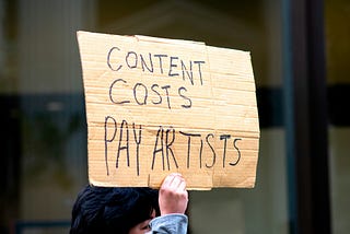 A sign reading “content costs pay artists”. Creativity and money are not mutually exclusive.