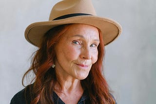 Portrait of an older red-haired women wearing a sun hat and smiling for the camera.