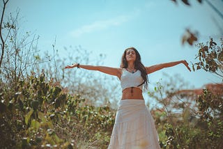 A woman dressed in white linen does a yoga pose in a field.