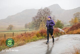 The author, at the time in his late 40s, running along a rural road while wearing a purple waterproof jacket and assorted other running gear. A mountain can be seen through misty rain behind, and the surface of the road is soaked with water.