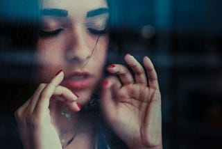a girl with dark hair and painted nails behind glass