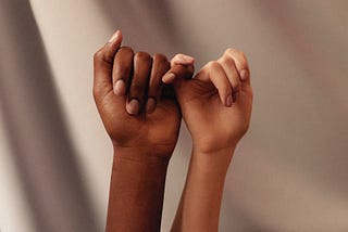 Hands of two women interlocking pinkies with one another.