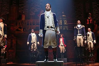 hamilton musical still with characters standing on chairs