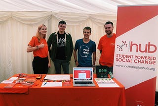 From left to right, Holly, Jordan, Jack and Tom are at the volunteering fayre, behind a table with leaflets on.