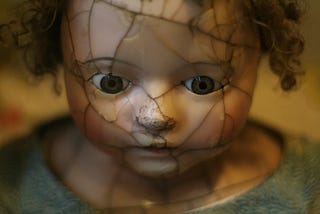 Porcelan doll face that is cracked and looking down and with the closed mouth, looking scared.