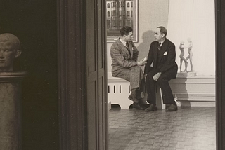 two-men-converse-in-an-open-doorway-to-a-gallery
