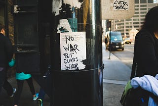 A handmade sticker reading “No war but class war” on a utility pole.