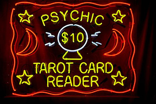 Neon sign reads “Psychic $10 Tarot Card Reader“ with moon and stars graphics and a picture of crystal ball