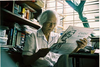 Nguyen’s grandfather reading a newspaper in writing corner, surrounded by books and papers.