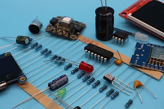 A collection of electronics components scattered on a surface, including capacitors, resistors, small displays, LEDs, transistors and other parts.