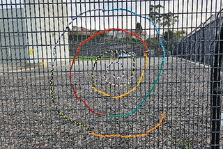 multi coloured threads woven into a swirl shape on a wire fence
