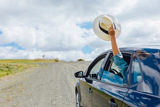 A car, driving down the road, an excited hand holding a hat, waving goodbye.