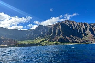 Hig cliffs in a backdrop with blue ocean waters in front are shown.