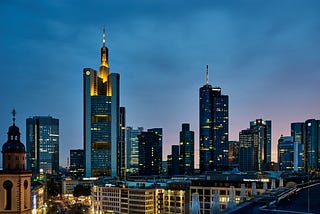 傍晚的法蘭克福金融區摩天大樓燈火輝映，老城教堂鐘塔靜立天際；國際化都市展現德國大學城與就業中心魅力，呼應留學德國、QS 排名探索及 TaiGer 對學生的升學導航，助你從申請到生活一次掌握。