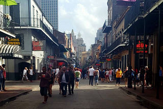 People walking down Bourbon Street surrounded by balconies neon signs and the echo of jazz in the heart of New Orleans