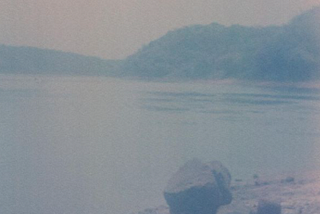 fotografia que retrata o rio Paraná, com vegetação ao fundo e uma pedra em primeiro plano