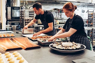 A man and a woman are cooking in a restaurant’s kitchen.