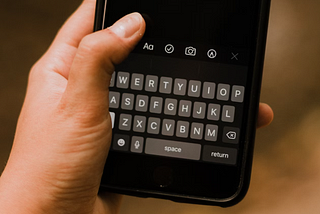 Mão utilizando celular com dedo encima de teclado na tela do dispositivo