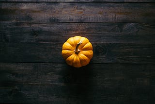 A photo from above of a small orange pumpkin on a dark brown wooden table top