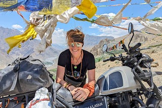 A woman leaning on the saddle of her bike with prayer flag fluttering in the wind above her head