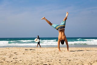 A man in board shorts doing a cartwheel on the beach.
