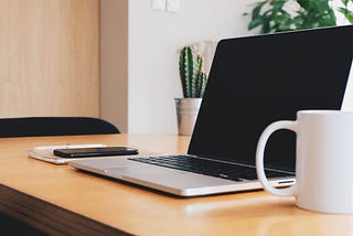 Laptop open on desk with white mug.