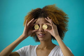 A woman holds up two bitcoins in front of her eyes so she cannot see.