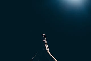 A dark background with a set of hands raised in prayer.