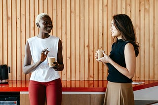 Two women holding paper coffee cups in conversation with one another.