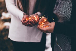 Close-up photo of two person holding lighted string lights.