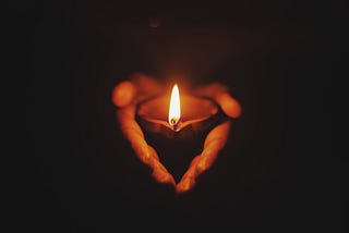 Two hands in shadow hold a candle with a bright burning flame