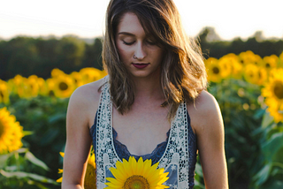 woman in field looking down at sunflower