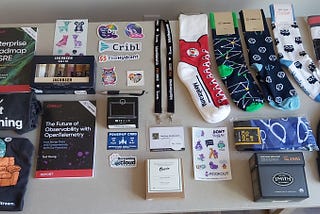 A table in a hotel room covered in socks, stickers, food, and books collected from various vendors throughout the conference