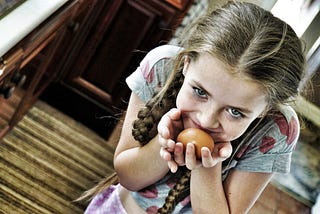 Little girl looking sneaky and holding an egg