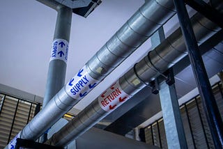 Two pipes running parallel to one another along a ceiling. One says “supply” and one “return.”