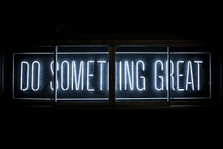 Neon sign lit up with “Do Something Great” against a black backdrop.