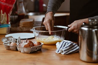A person stirs a yellow substance in a clear bowl. Egg shells are in a carton on the counter. Mom’s Lemon Meringue Pie by Jim Latham | Photo by Sincerely Media on Unsplash