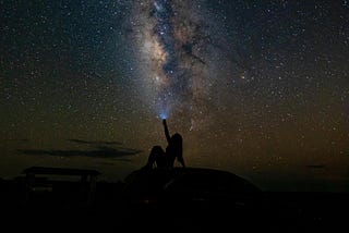 Silhouette of a woman sitting under a starry night sky.