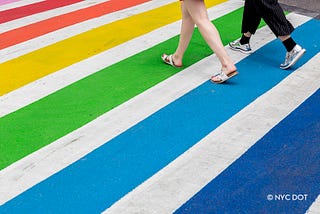 Two pairs of feet walking across a rainbow-striped crosswalk
