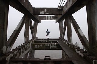 A person somersaulting over a bridge over a lake.