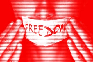 Woman with paper pressed tightly over her mouth that reads “freedom”.