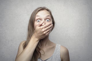 Woman in grey shirt covering her mouth and looking surprised